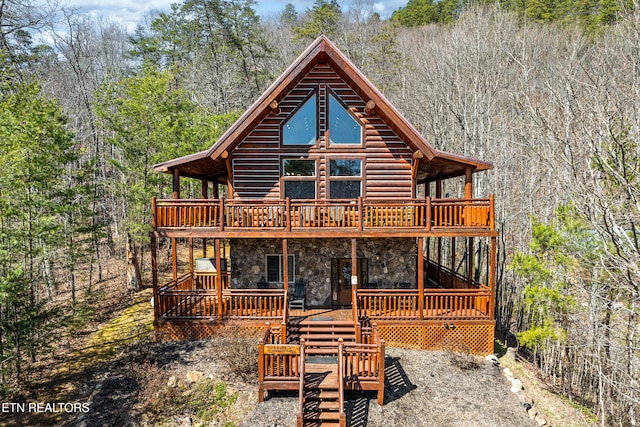 back of house featuring a forest view, a wooden deck, stone siding, and log siding