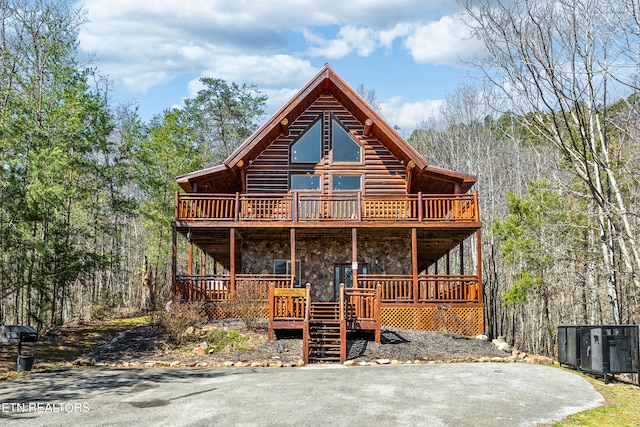 log home featuring central air condition unit, a forest view, stone siding, and a wooden deck