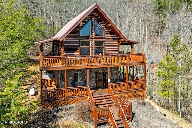 log cabin with stairs, a wooded view, stone siding, and a wooden deck