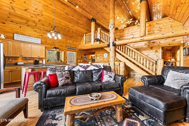 living room featuring light wood finished floors, wooden walls, wood ceiling, and stairs