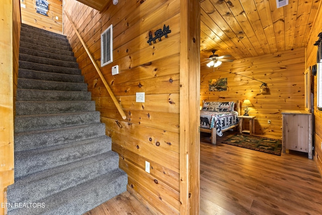 staircase featuring visible vents, wood finished floors, wooden ceiling, wood walls, and ceiling fan