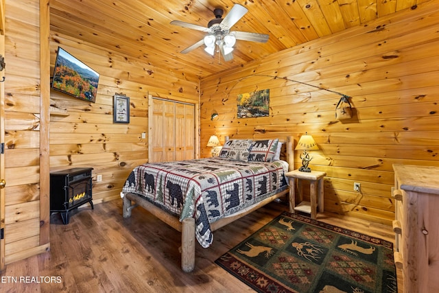 bedroom with a ceiling fan, wood finished floors, a wood stove, wood ceiling, and wood walls