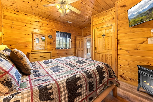 bedroom featuring wooden ceiling, a wood stove, wooden walls, and wood finished floors