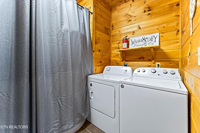 clothes washing area with tile patterned flooring, wooden walls, washing machine and dryer, and laundry area