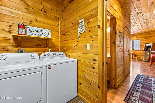 clothes washing area featuring wooden walls, wood ceiling, laundry area, light wood-style floors, and washer and dryer