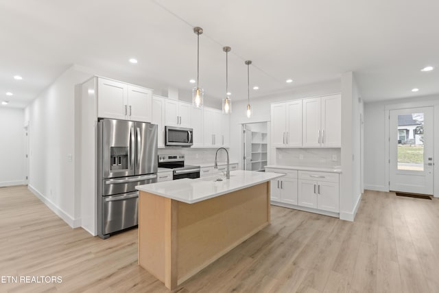 kitchen with a sink, stainless steel appliances, light wood-style floors, and decorative backsplash