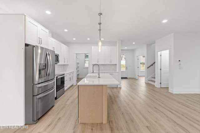 kitchen with a center island with sink, a sink, light wood-style floors, appliances with stainless steel finishes, and light countertops