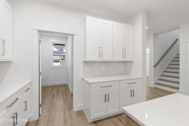 kitchen with tasteful backsplash, white cabinets, light wood-type flooring, and light countertops