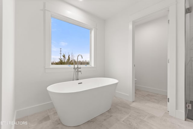 full bathroom featuring a soaking tub, toilet, and baseboards