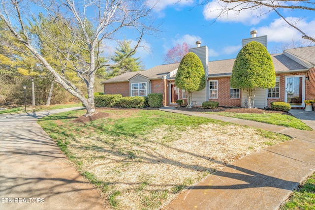 view of front of property with a front lawn, brick siding, and a chimney