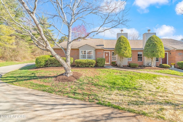 ranch-style house featuring driveway, brick siding, a chimney, and a front lawn