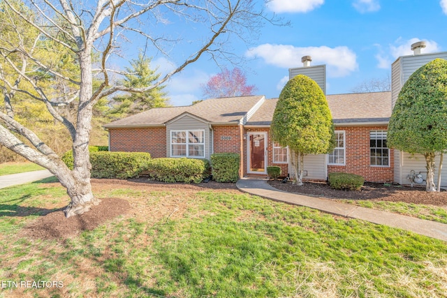 single story home with a shingled roof, a front yard, brick siding, and a chimney