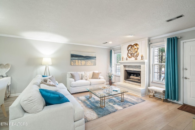 living area with visible vents, light wood finished floors, a fireplace with raised hearth, a textured ceiling, and crown molding