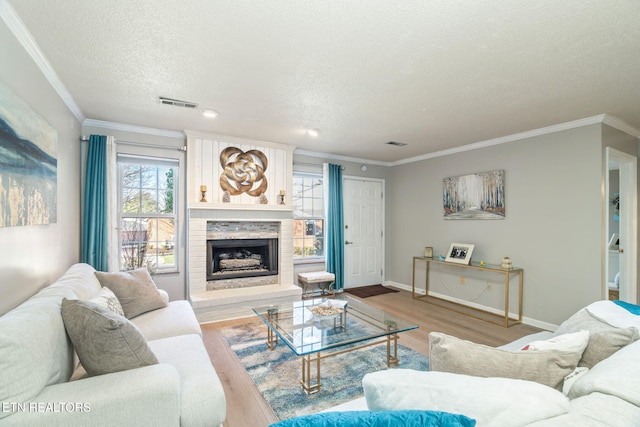 living room featuring visible vents, a fireplace with raised hearth, wood finished floors, crown molding, and baseboards