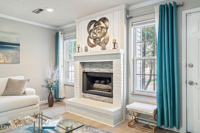 living room with a healthy amount of sunlight, wood finished floors, visible vents, ornamental molding, and a brick fireplace