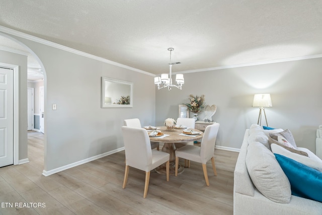 dining room featuring a textured ceiling, ornamental molding, arched walkways, and light wood-type flooring