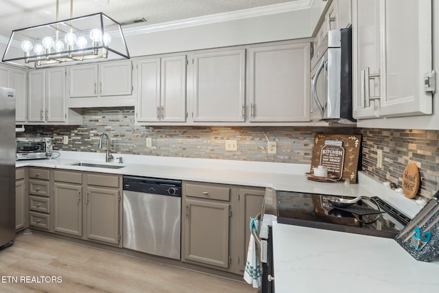 kitchen with tasteful backsplash, gray cabinetry, ornamental molding, stainless steel appliances, and a sink