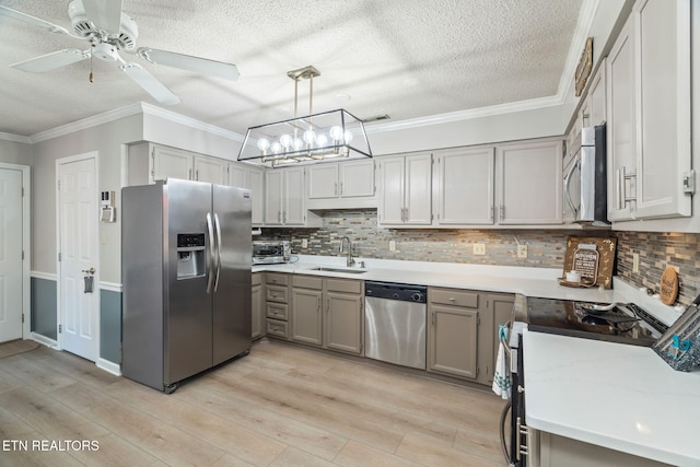 kitchen with light wood finished floors, gray cabinetry, ornamental molding, stainless steel appliances, and a sink