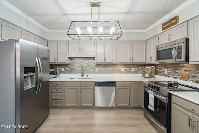 kitchen with ornamental molding, stainless steel appliances, light countertops, and a sink