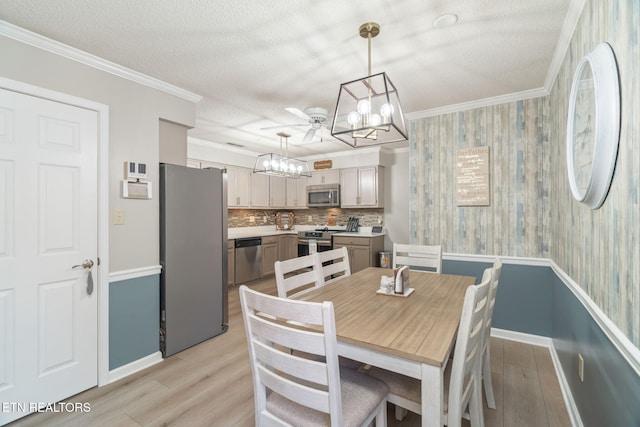 dining room featuring a textured ceiling, light wood-style flooring, a notable chandelier, and ornamental molding