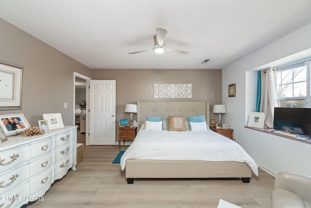 bedroom featuring visible vents, baseboards, ceiling fan, light wood-type flooring, and a textured ceiling