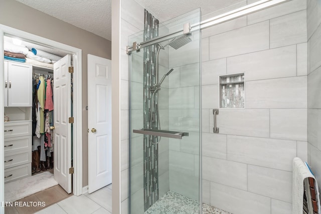 bathroom with tile patterned flooring, a shower stall, a spacious closet, and a textured ceiling