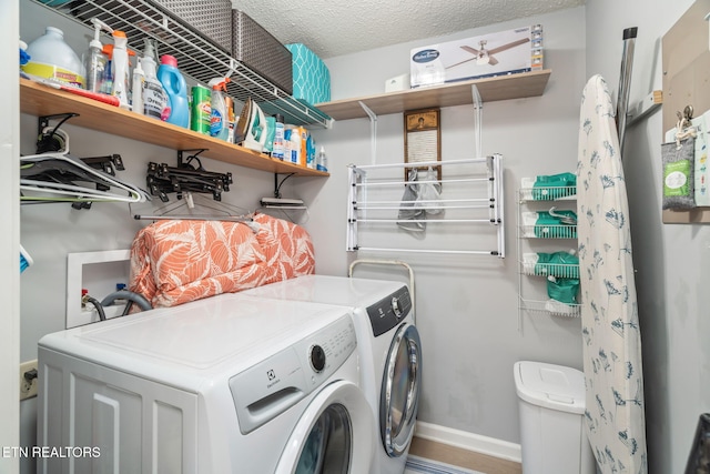 clothes washing area with laundry area, washing machine and dryer, baseboards, and a textured ceiling