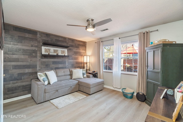 living room with wooden walls, a ceiling fan, visible vents, light wood-style floors, and an accent wall