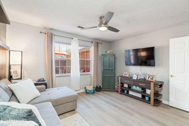 living area with visible vents, baseboards, ceiling fan, light wood-type flooring, and a textured ceiling