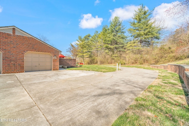 view of side of property featuring a yard, brick siding, a garage, and concrete driveway