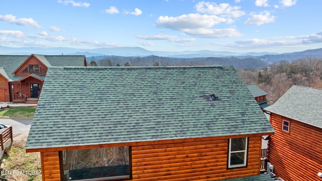 view of side of home with log veneer siding, a mountain view, and roof with shingles