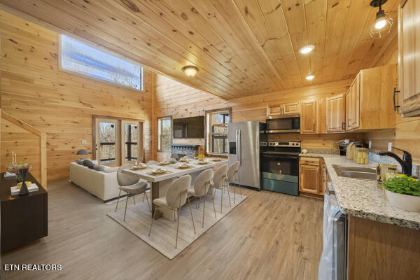 kitchen featuring wooden walls, wooden ceiling, light wood-style flooring, appliances with stainless steel finishes, and a sink