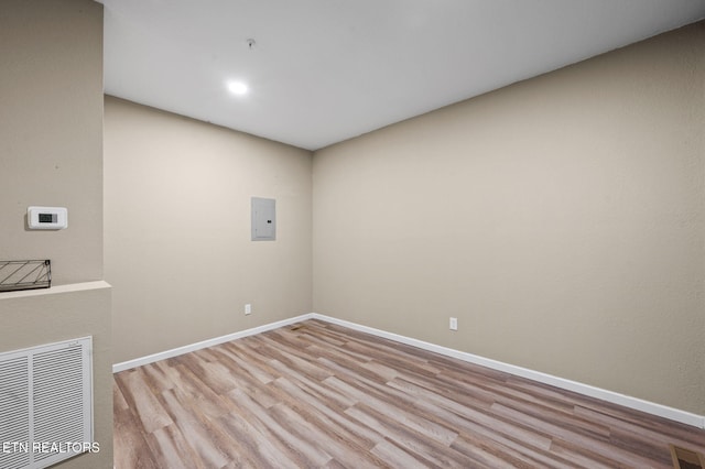 empty room with electric panel, baseboards, visible vents, and light wood finished floors