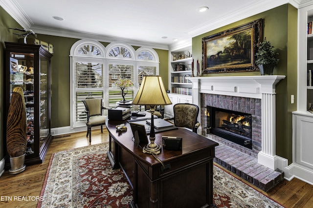 home office with built in shelves, ornamental molding, wood finished floors, baseboards, and a brick fireplace