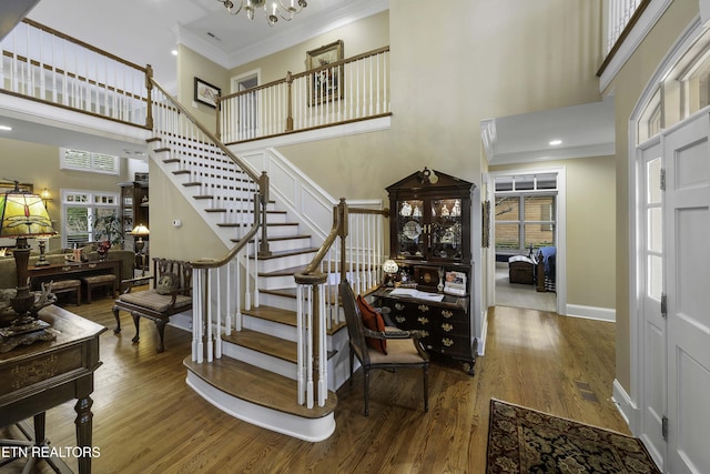 entryway featuring a notable chandelier, stairway, crown molding, and wood finished floors