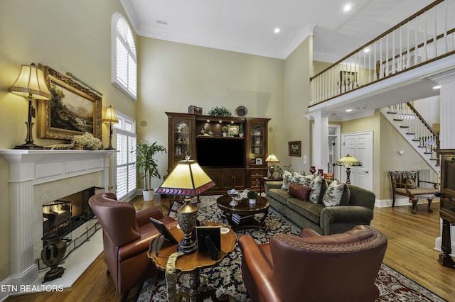 living room with stairs, ornamental molding, a fireplace, a towering ceiling, and wood finished floors