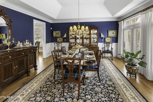 dining room with a raised ceiling, wood finished floors, a wainscoted wall, and a chandelier