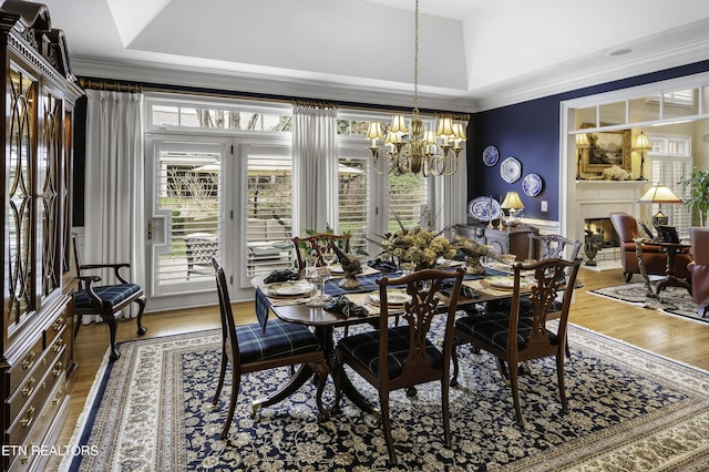 dining space with a chandelier, ornamental molding, a raised ceiling, and wood finished floors