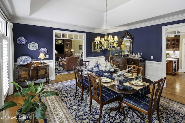 dining space with an inviting chandelier, ornamental molding, wood finished floors, and wainscoting