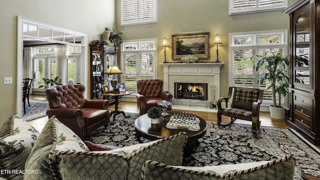 living room featuring a high ceiling, a warm lit fireplace, and wood finished floors