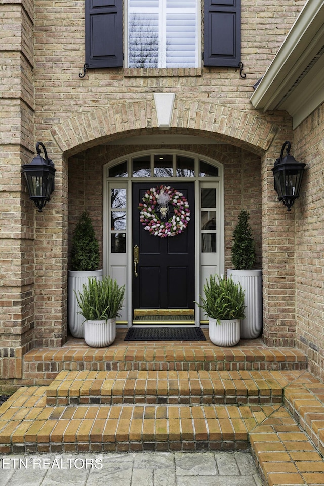 entrance to property with a porch and brick siding