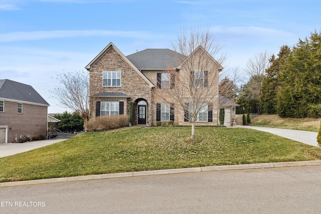 traditional home with brick siding, a front yard, a garage, stone siding, and driveway