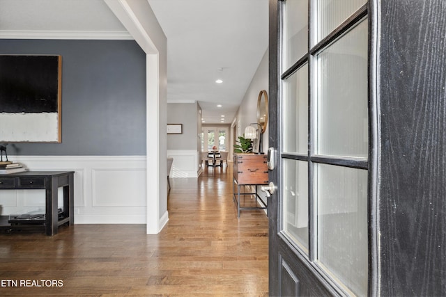 corridor with a decorative wall, recessed lighting, wood finished floors, ornamental molding, and wainscoting