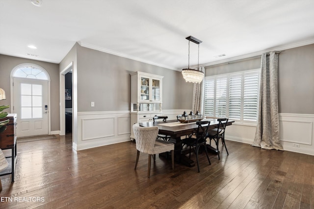 dining area with visible vents, dark wood finished floors, ornamental molding, a decorative wall, and a notable chandelier