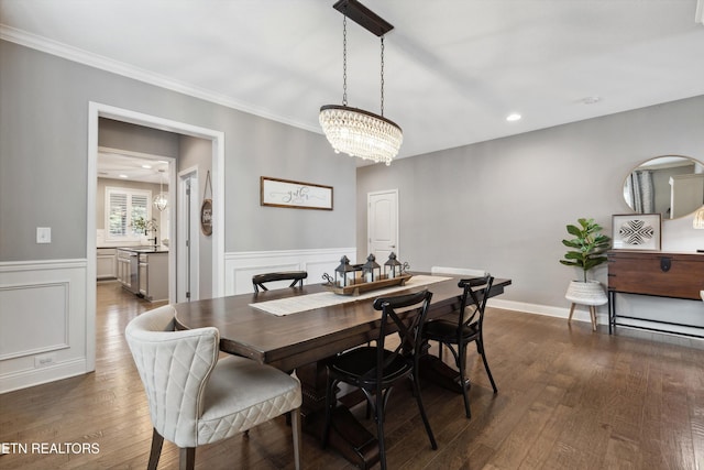 dining space featuring a wainscoted wall, ornamental molding, dark wood finished floors, and a notable chandelier