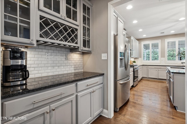 kitchen featuring hardwood / wood-style flooring, dark stone counters, stainless steel appliances, and decorative backsplash