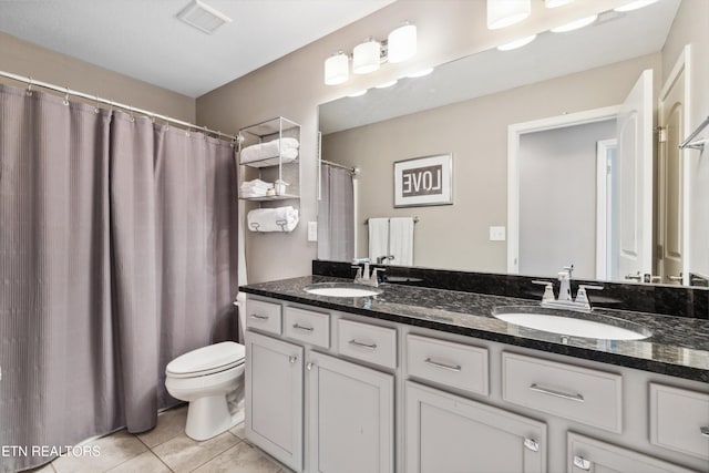 full bathroom featuring toilet, double vanity, a sink, and tile patterned floors