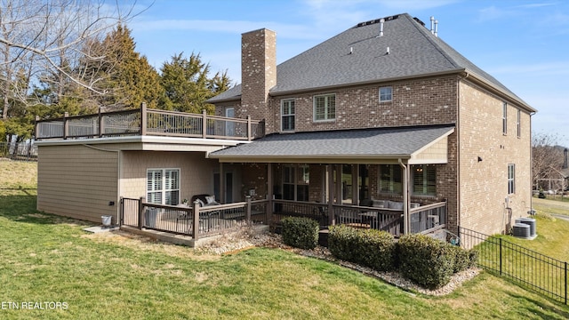 back of property featuring roof with shingles, brick siding, a chimney, a lawn, and fence