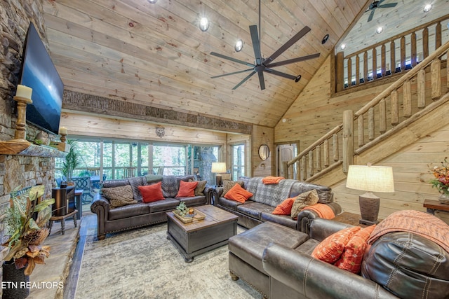 living room featuring wooden walls, wood ceiling, stairway, a stone fireplace, and high vaulted ceiling