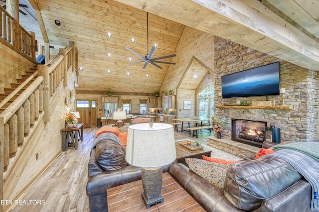 living area with light wood-type flooring, wood walls, a wealth of natural light, and a stone fireplace